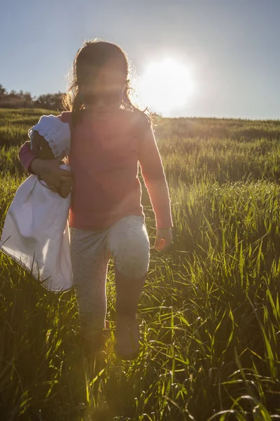 Menina e sua boneca andando através do campo de cereais verde em s — Fotografia de Stock