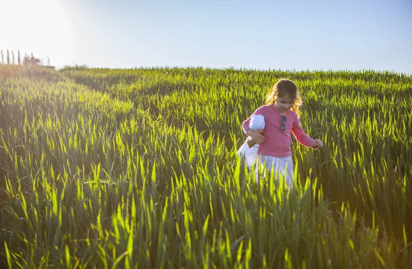 Niña y su muñeca caminando por el campo de cereales verde en s — Foto de Stock