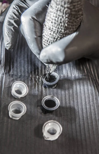 Tattoo artist refilling pen from ink poured into small cups — Stock Photo, Image