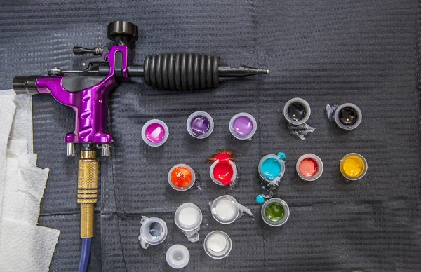 Table de tatoueur avec plusieurs petites tasses et machine à encre pistolet — Photo