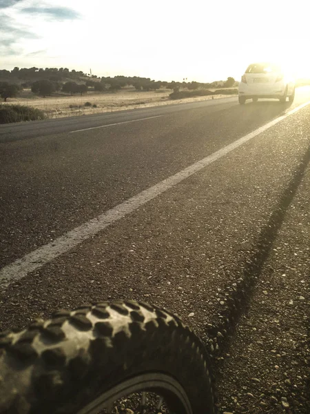 Carro ultrapassando uma bicicleta de montanha na estrada local ao pôr do sol — Fotografia de Stock
