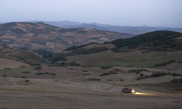 Mountain landscape at dusk with combine harvester working — Stock Photo, Image