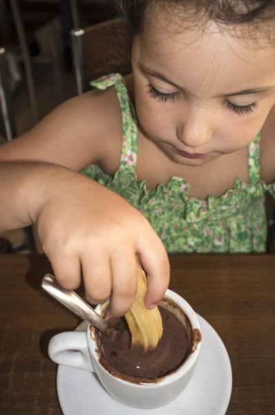 Cute little girl eating churros with hot chocolate — Stock Photo, Image