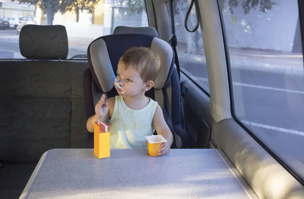 Маленький хлопчик сидить у фургоні та їсть йогурт та апельсиновий сік — стокове фото