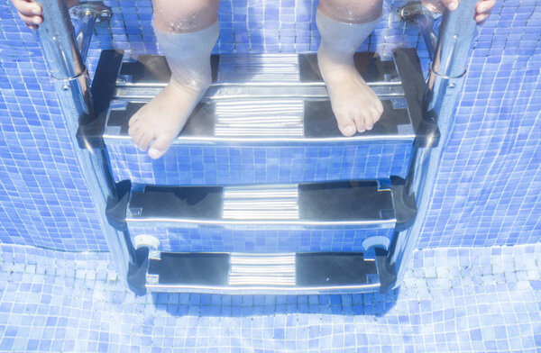 Ребенок сидит на лестнице бассейна с ногами underwa
