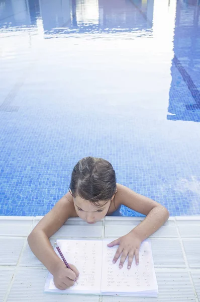 Gyermek lány csinál nyaralás házi feladatot, mint úszás medence — Stock Fotó