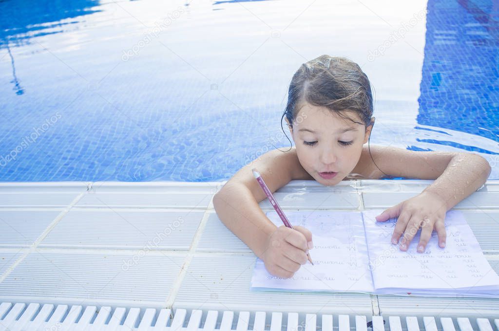 Child girl doing holidays homework over swimming poolside