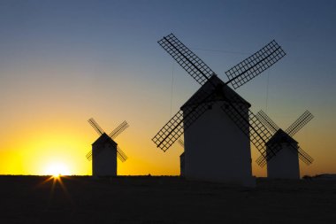 Silhouettes of traditional windmills at Campo de Criptana site, Spain. Rising backlighing clipart