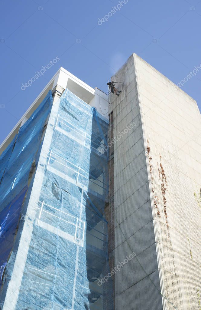 Rope access technician washing building facade