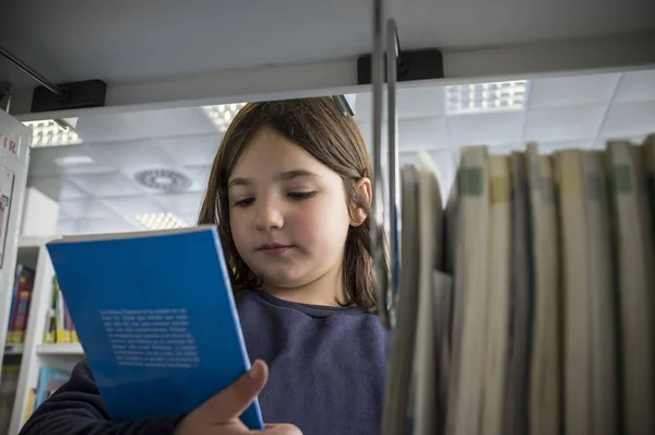 Ung flicka välja böcker från bibliotek bokhylla — Stockfoto