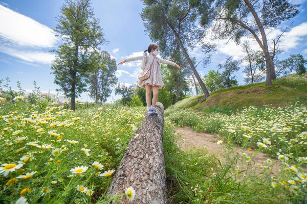 デイジーフィールドの真ん中の丸太の上を歩いている少女 顔のマスクをしてる — ストック写真