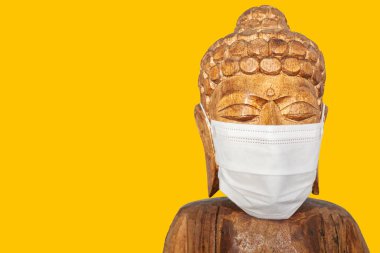 Yüz maskesi takan Buda heykeli. Sarı üzerinde izole edilmiş. Covid-19 konsepti