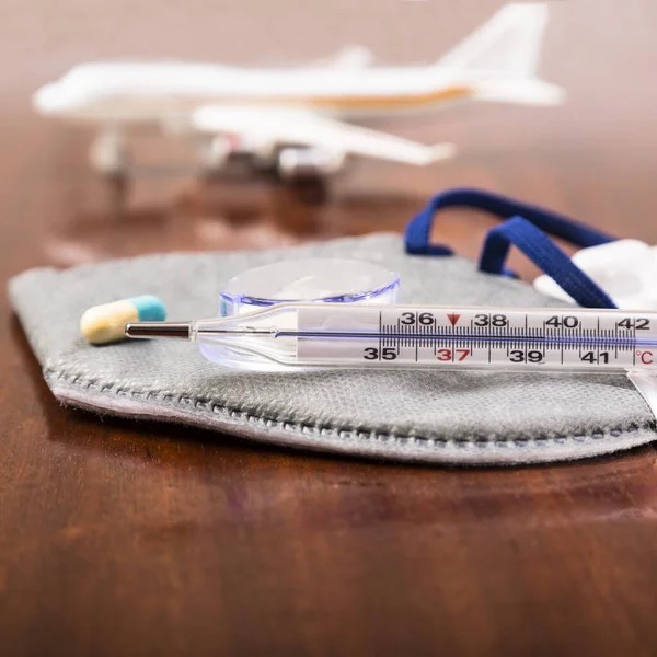 Thermometer, mask, medicine on the background of the plane