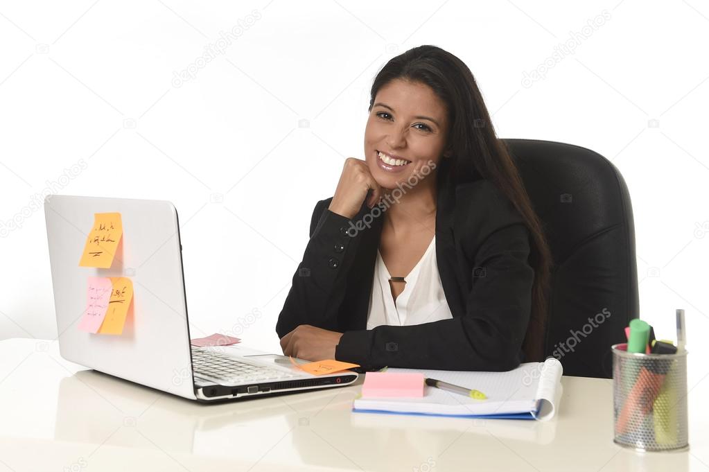 attractive hispanic businesswoman sitting at office desk working on computer laptop smiling happy