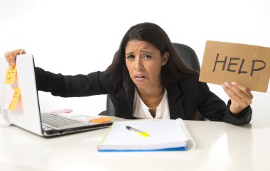 young busy desperate Latin businesswoman holding help sign sitting at office desk in stress worried