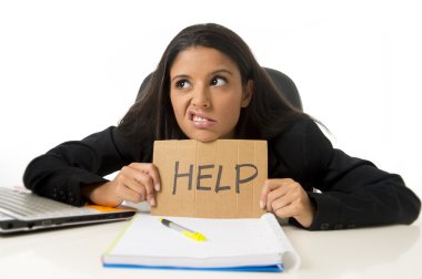 young busy desperate Latin businesswoman holding help sign sitting at office desk in stress worried