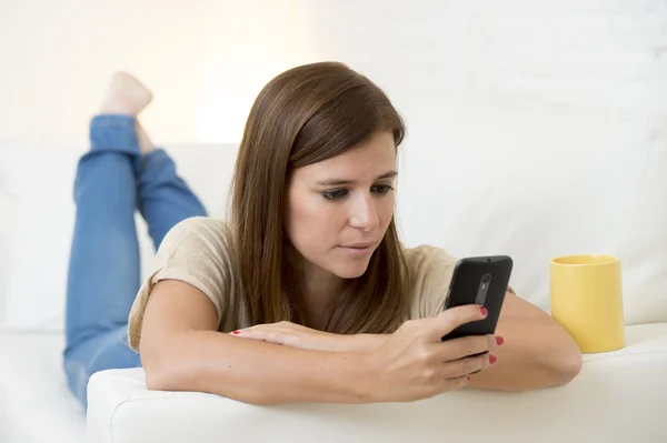 Wanita cantik dengan kopi bahagia di sofa SMS jaringan pada ponsel santai — Stok Foto