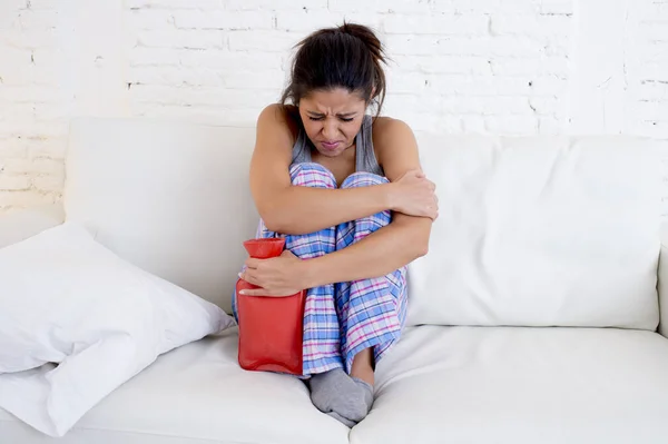 Young beautiful hispanic woman holding hot water bottle against belly suffering menstrual period pain — Stock Photo, Image