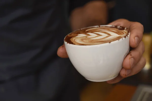 Manos presentando delicioso café con crema de leche espuma decorativa en taza — Foto de Stock