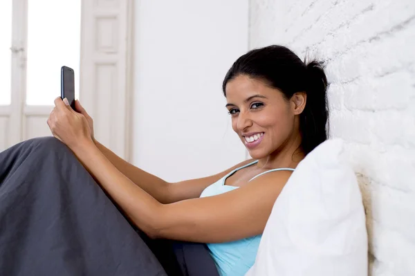 Hispánský žena uvolněná, pomocí internetu mobilní telefon odesílání zprávy na domácí ložnice usmíval se šťastný — Stock fotografie