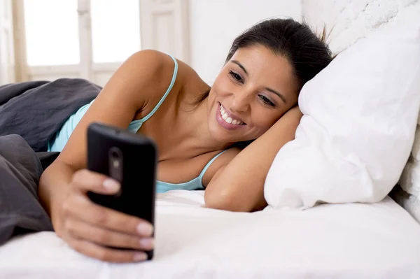 Hispânico mulher relaxado usando internet telefone celular enviando mensagem em casa quarto sorrindo feliz — Fotografia de Stock