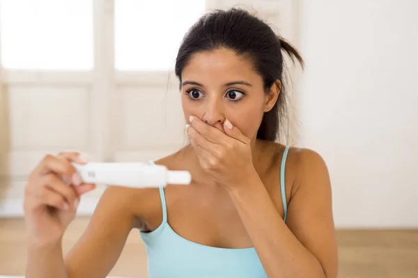 Donna latina che tiene test di gravidanza a letto a casa guardando risultato positivo in shock e stress — Foto Stock