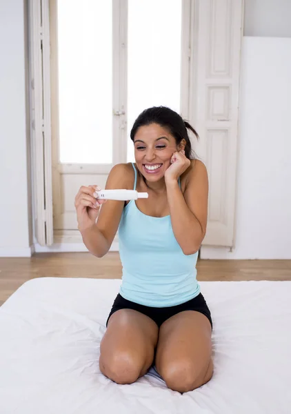 Hermosa mujer latina sosteniendo prueba de embarazo buscando y encontrando resultado positivo sonriendo feliz y emocionado — Foto de Stock