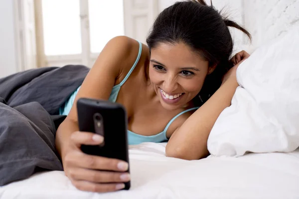 Mulher hispânica na cama mensagens internet surf no telefone celular em vício em rede social — Fotografia de Stock