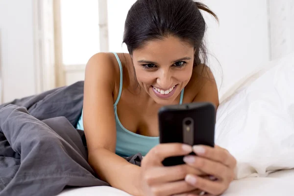 Mulher hispânica na cama mensagens internet surf no telefone celular em vício em rede social — Fotografia de Stock