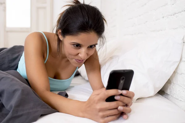 Donna ispanica a letto che invia SMS a internet navigando sul cellulare nella dipendenza dai social network — Foto Stock