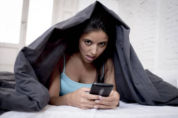 Jeune belle hispanique téléphone portable femme accro au lit avec couverture au-dessus de la tête textos internet surf — Photo