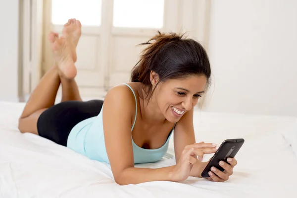İspanyol kadın mobil internet kullanımı rahat telefon ev yatak mutlu gülümseyerek, gönderme mesaj — Stok fotoğraf