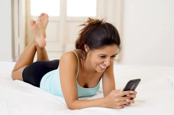 Donna ispanica rilassato utilizzando internet cellulare invio di messaggi a casa camera da letto sorridente felice — Foto Stock