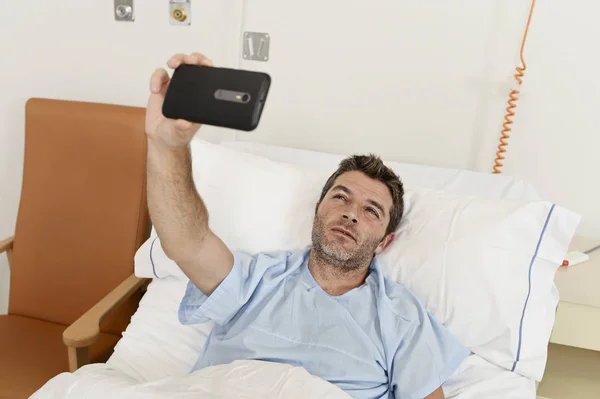 Muž ležící na posteli nemocnice klinika držení mobilního telefonu s autoportrét selfie fotografii smutné, depresivní — Stock fotografie