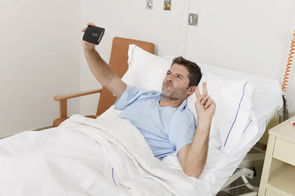 魅力的な男性が仰向けになってベッド病院セルフ ポートレート selfie 写真を撮る携帯電話を保持しています。 — ストック写真