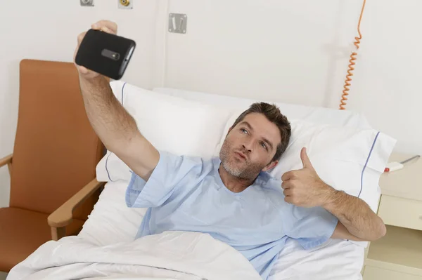 Homem atraente deitado na cama hospital clínica segurando telefone celular tendo auto retrato selfie foto — Fotografia de Stock