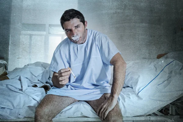 Joven atractivo hombre buscando triste preocupado en hospital cama fumar —  Fotos de Stock
