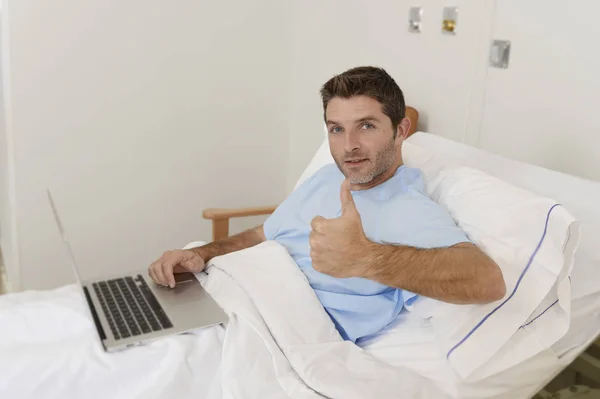 Пациент в больнице страдает болезнью и работает на койке клиники с ноутбука компьютер улыбается счастливым — стоковое фото