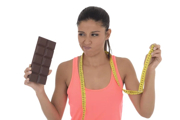 Jovem atraente mulher latina segurando taylor fita métrica e barra de chocolate na dieta nutricional saudável — Fotografia de Stock