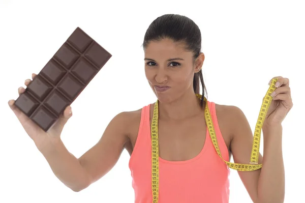 Young attractive latin woman holding taylor measure tape and chocolate bar in healthy nutrition diet — Stock Photo, Image