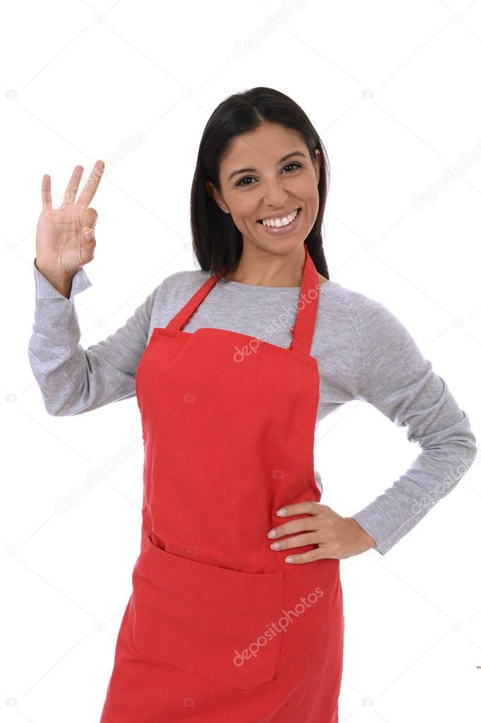 corporate portrait of young attractive hispanic home cook woman in red apron posing happy and smiling isolated