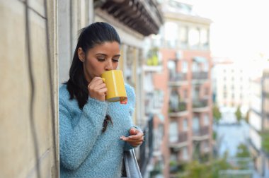 latin kadın fincan kahve ya da çay gülümseyerek mutlu daire pencere balkon içme 