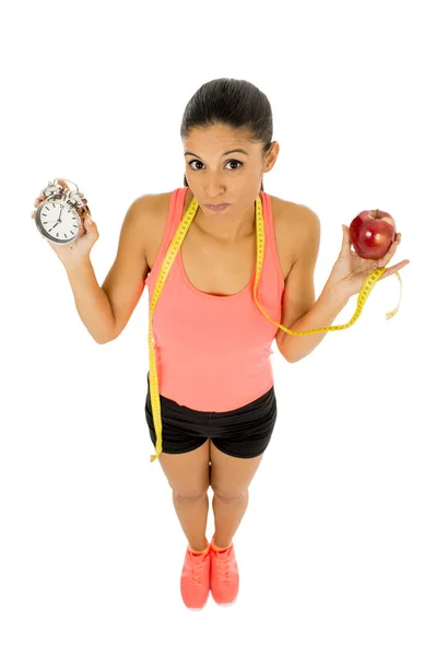 Beautiful and fit hispanic woman holding alarm clock apple fruit and taylor measure tape — Stock Photo, Image