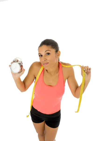 Hispanic woman holding alarm clock and taylor measure tape in time for sport and diet concept — Stock Photo, Image