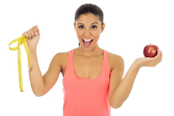 Mujer latina deportiva en ropa de fitness sosteniendo fruta de manzana y cinta métrica sonriendo feliz — Foto de Stock