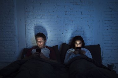 Çift evde cep telefonuyla ilişki iletişim sorunu içinde gece geç yatakta