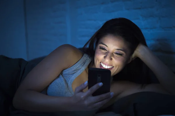 Κοπέλα στο κρεβάτι χρησιμοποιώντας κινητό τηλέφωνο αργά τη νύχτα σκοτεινή κρεβατοκάμαρα ψέματα χαρούμενη και χαλαρή — Φωτογραφία Αρχείου