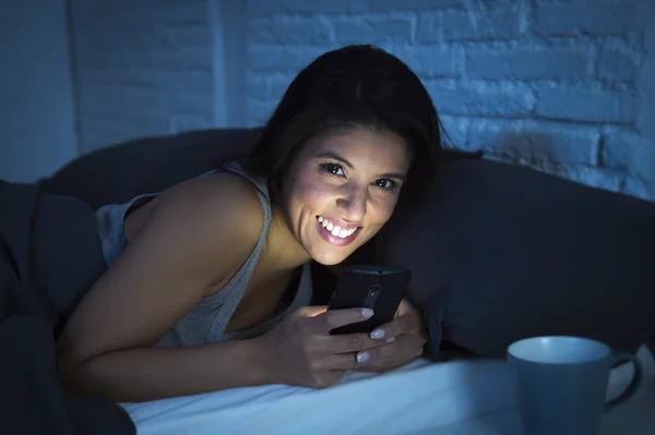 Menina na cama usando telefone celular tarde da noite no quarto escuro deitado feliz e relaxado — Fotografia de Stock