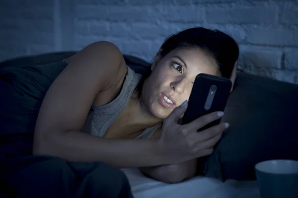 Дівчина в ліжку, використовуючи мобільний телефон пізно вночі в темній спальні лежить щасливий і розслаблений — стокове фото
