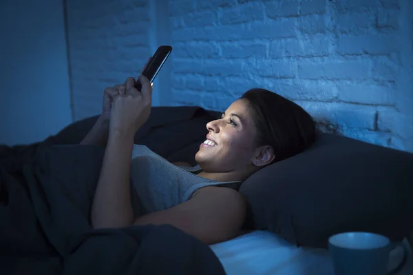 Κοπέλα στο κρεβάτι χρησιμοποιώντας κινητό τηλέφωνο αργά τη νύχτα σκοτεινή κρεβατοκάμαρα ψέματα χαρούμενη και χαλαρή — Φωτογραφία Αρχείου